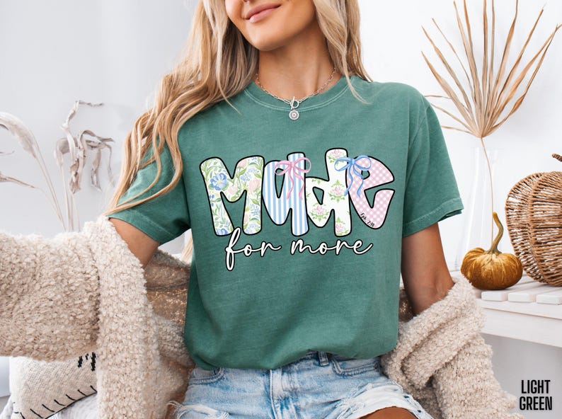 Op de afbeelding: Lichtgroen T-shirt met de tekst "MADE for more" in een kleurrijk ontwerp met bloemen- en streepmotieven. Het shirt is een casual stijl, geschikt voor dagelijks gebruik. De tekst is in een speels lettertype.
