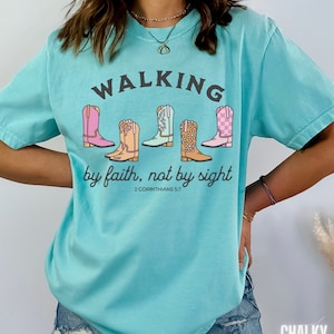 Puede incluir: Una camiseta azul turquesa con un gr&aacute;fico de cinco botas de vaquero de colores y el texto "WALKING by faith, not by sight 2 CORINTHIANS 5:7".
