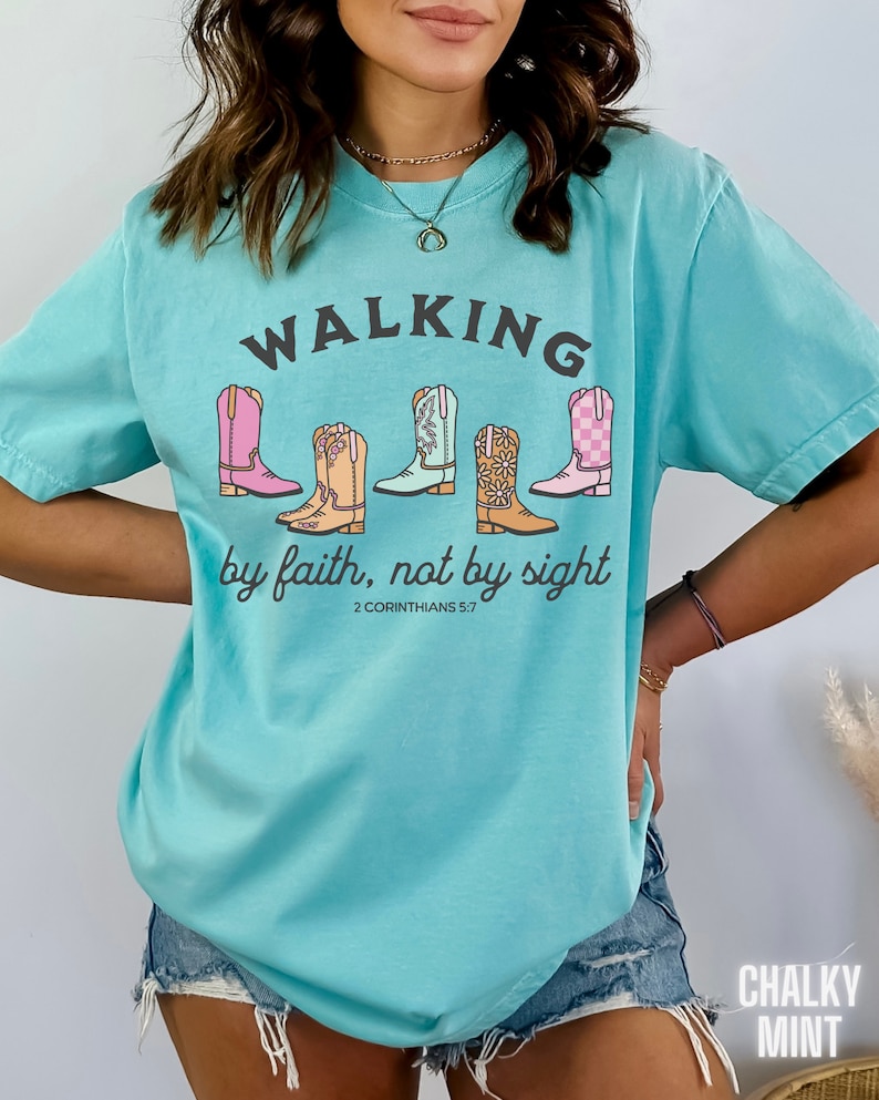 Puede incluir: Una camiseta azul turquesa con un gr&aacute;fico de cinco botas de vaquero de colores y el texto "WALKING by faith, not by sight 2 CORINTHIANS 5:7".