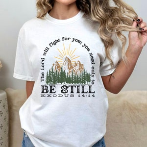 May include: White t-shirt with a mountain scene and the text "The Lord will fight for you; you need only to BE STILL EXODUS 14:14"