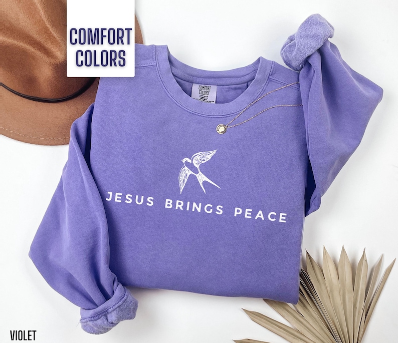May include: A purple sweatshirt with the text "Jesus Brings Peace" and a white bird design. The sweatshirt is made of a soft, comfortable fabric.