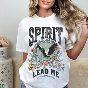 K&ouml;nnte beinhalten: Wei&szlig;es T-Shirt mit einem grafischen Aufdruck eines fliegenden Vogels mit Blumen und dem Text "SPIRIT LEAD ME".