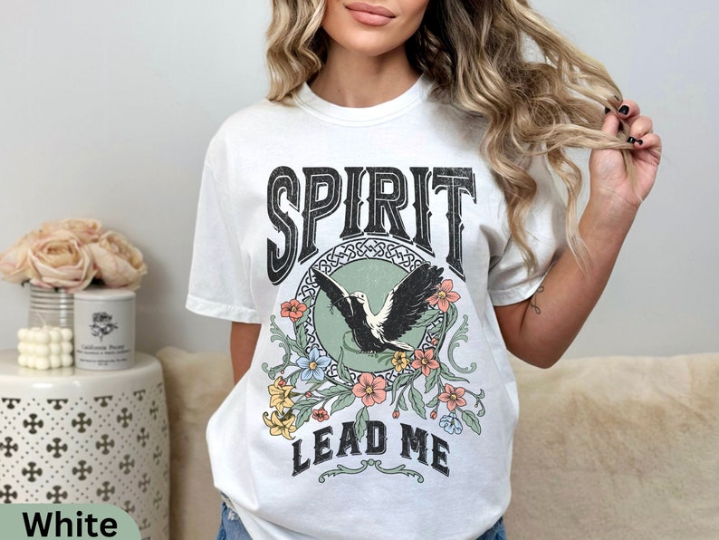 K&ouml;nnte beinhalten: Wei&szlig;es T-Shirt mit einem grafischen Aufdruck eines fliegenden Vogels mit Blumen und dem Text "SPIRIT LEAD ME".