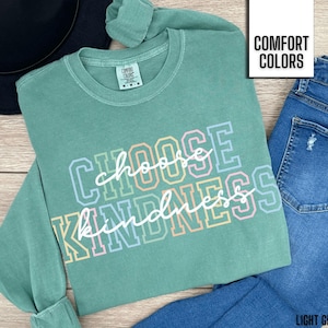 May include: A light green long-sleeved t-shirt with the text "Choose Kindness" in rainbow colors. The shirt is made of a soft, comfortable fabric and has a relaxed fit.