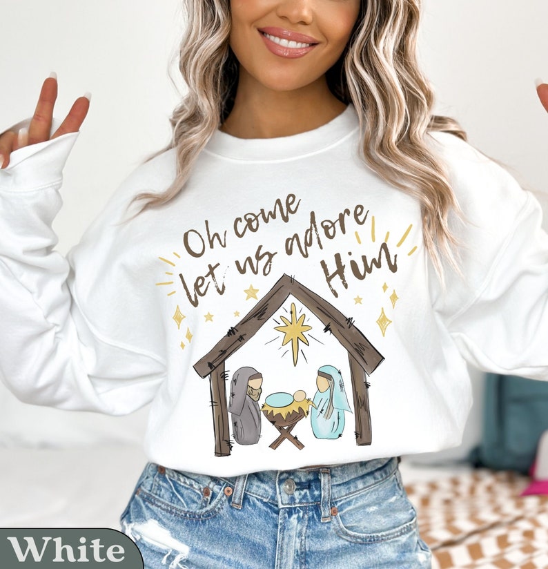 Puede incluir: Sudadera blanca con un gr&aacute;fico de la natividad de Navidad y el texto "Oh come let us adore Him".