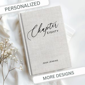 May include: A light gray hardcover journal with the words "Chapter Eighty" in elegant black script. The name "Jean Jenkins" is printed below. The word "PERSONALIZED" is at the top, and "MORE DESIGNS" is at the bottom.
