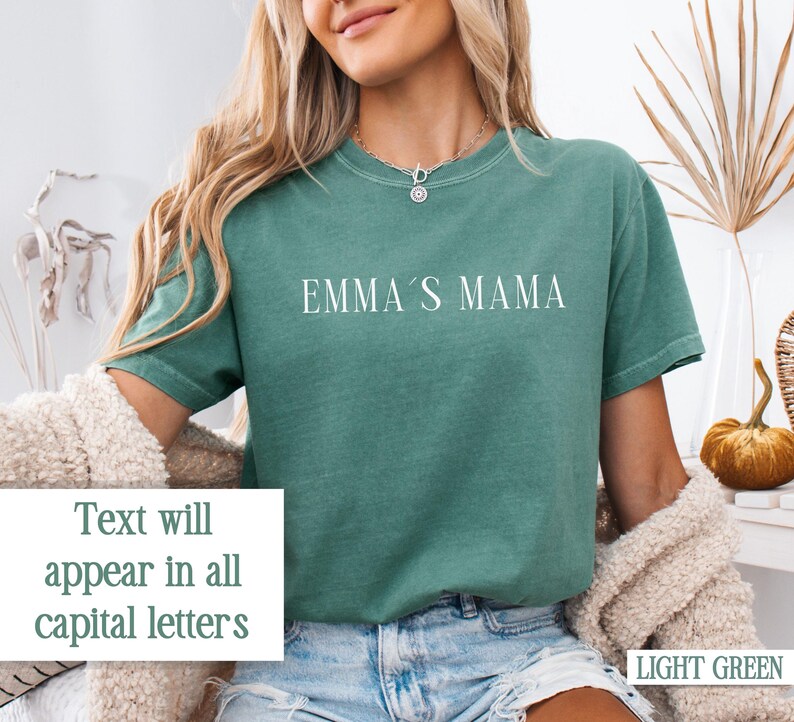 May include: A light green t-shirt with the text "EMMA'S MAMA" printed in white on the front. The text will appear in all capital letters.