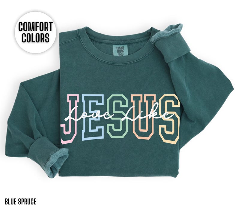 May include: A dark green sweatshirt with the word "JESUS" in rainbow coloured letters and the words "Love Like" written in white script underneath. The sweatshirt is made of a soft, comfortable material.
