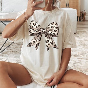 Puede incluir: Una camiseta blanca con un gran lazo de estampado de leopardo.