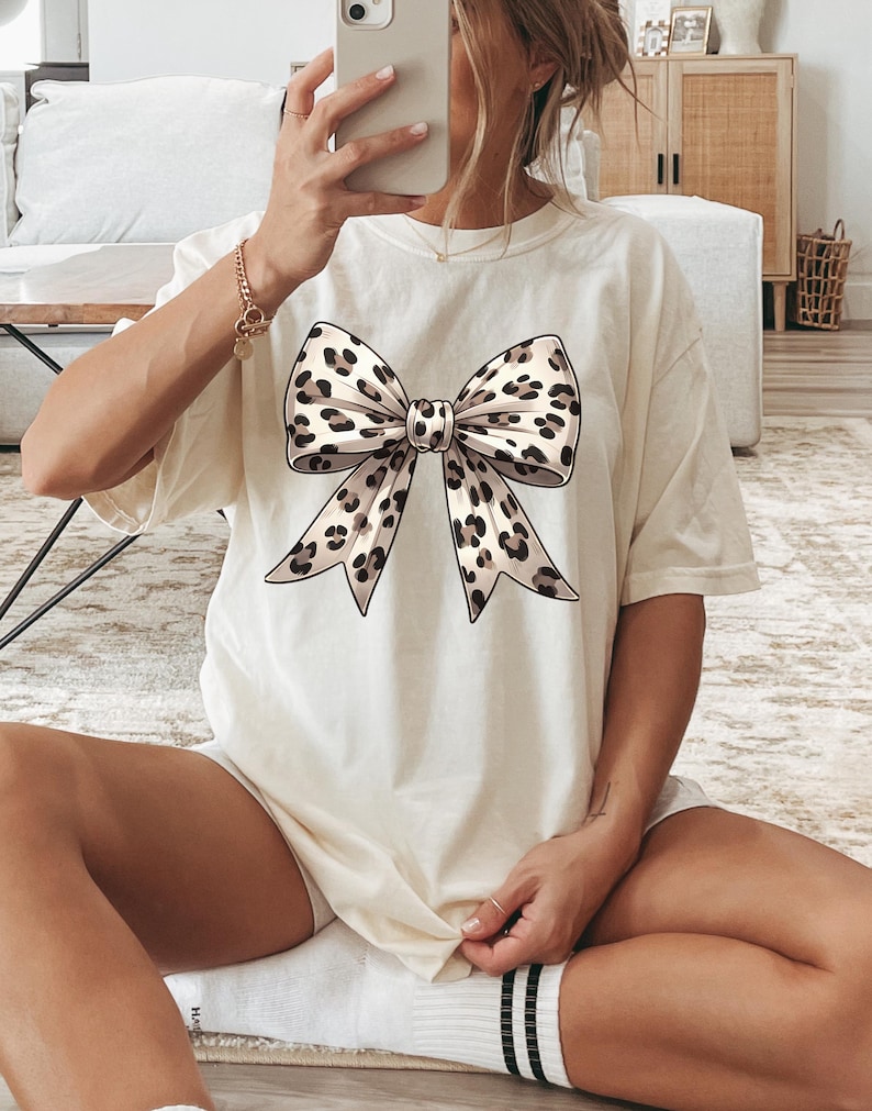 Puede incluir: Una camiseta blanca con un gran lazo de estampado de leopardo.