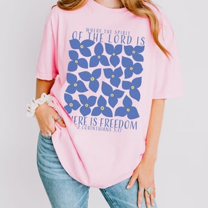 May include: Pink t-shirt with a blue floral design and the text "Where the Spirit of the Lord is, there is freedom. 2 Corinthians 3:17"