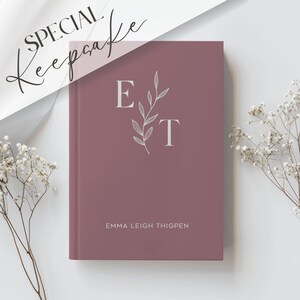 Może przedstawiać: Dziennik w kolorze pudrowego r&oacute;żu z białym wzorem kwiatowym i inicjałami "E" i "T" na okładce. Imię "Emma Leigh Thigpen" jest nadrukowane na biało na dole okładki.