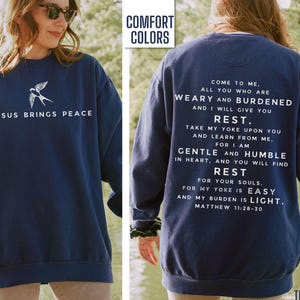 May include: Navy blue sweatshirt with a white bird graphic and the text "Jesus Brings Peace" on the front. The back of the sweatshirt has a white text quote from Matthew 11:28-30, "Come to me, all you who are weary and burdened and I will give you rest. Take my yoke upon you and learn from me, for I am gentle and humble in heart, and you will find rest for your souls. For my yoke is easy and my burden is light."