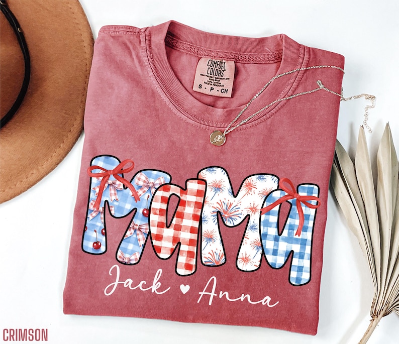 May include: A red Comfort Colors t-shirt with the word "MAMA" in a patriotic design. The letters are decorated with gingham, fireworks, and bows. The names "Jack" and "Anna" are written below the word "MAMA". A gold necklace is draped across the shirt.