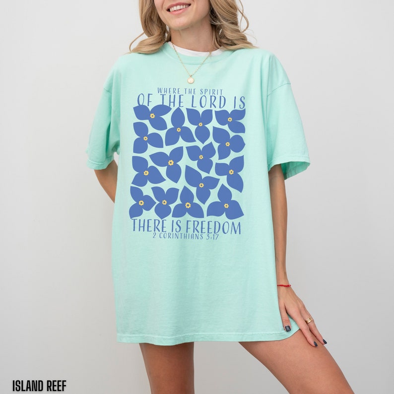 May include: A light blue t-shirt with a graphic design of blue flowers and the text "Where the spirit of the Lord is there is freedom 2 Corinthians 3:17".