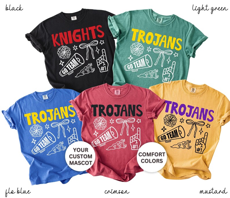 Puede incluir: Cinco camisetas de manga corta en negro, verde claro, azul, carmes&iacute; y mostaza. Cada camiseta presenta un gr&aacute;fico serigrafiado con un meg&aacute;fono, pomp&oacute;n, lazo, bander&iacute;n y dedo de espuma, junto con el texto KNIGHTS o TROJANS y GO TEAM.
