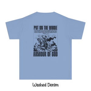 May include: A light blue t-shirt with a black graphic print of a knight on a horse. The graphic includes the text "Put on the whole armour of God" and a bible verse. The shirt is made of a washed denim fabric.