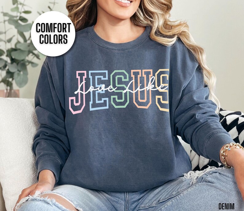 May include: A navy blue sweatshirt with the text "Jesus" in rainbow colours and the words "look like" in white script underneath. The sweatshirt is made of a soft, comfortable material and has a relaxed fit.