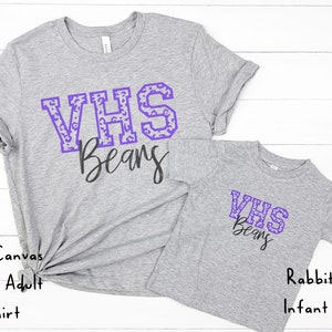 May include: Two gray t-shirts with the text "VHS Beans" in purple with a leopard print pattern. The larger shirt is a Bella Canvas Unisex Adult T-shirt. The smaller shirt is a Rabbit Skins Infant T-shirt.