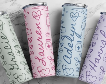 May include: Three stainless steel tumblers with a medical theme. The tumblers are pink, blue, and purple with a white background. Each tumbler has a different name on it: Lauren, Adelyn, and Hanna. The tumblers are decorated with medical symbols such as hearts, stethoscopes, and syringes.