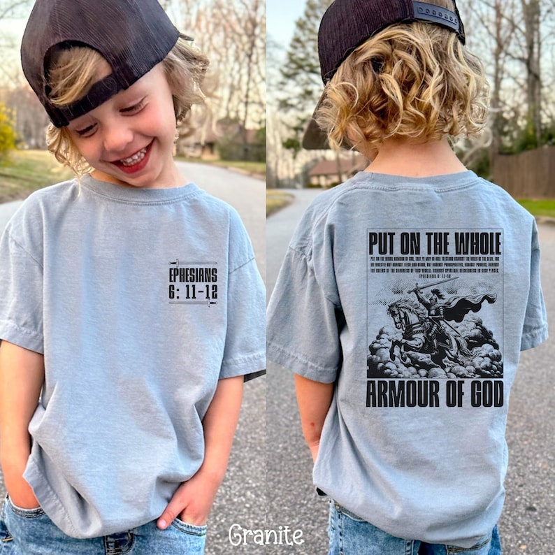 May include: A light blue t-shirt with a black graphic on the back that says "Put on the whole armour of God" and a scripture reference. The front of the shirt has the text "Ephesians 6:11-12" in black.