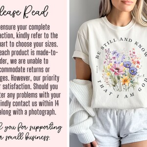 May include: A white t-shirt with a floral design and the text "Be Still and Know That I Am God" in a circle. The shirt is being worn by a person with a white cardigan and white shorts.