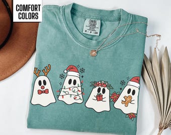May include: Light green t-shirt with a Christmas ghost design. The ghosts are wearing Santa hats, reindeer antlers, and a wreath. The text "COMFORT COLORS" is printed on the top left corner of the shirt.