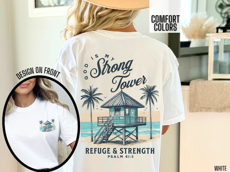 Puede incluir: Camiseta blanca con un gr&aacute;fico de una escena de playa con una torre de salvavidas y palmeras. El texto "God is my Strong Tower" est&aacute; escrito en una fuente cursiva sobre la torre. El texto "Refuge & Strength Psalm 61:3" est&aacute; escrito debajo de la torre.