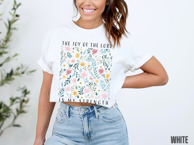 Op de afbeelding: Wit kort T-shirt met een bloemenpatroon en de tekst "The Joy of the Lord is My Strength".