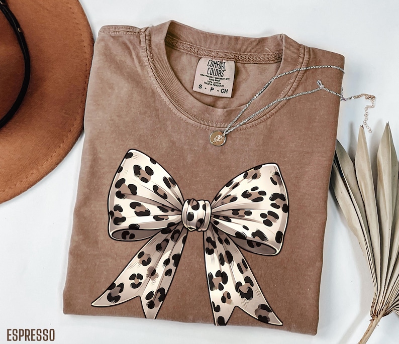 Puede incluir: Una camiseta marr&oacute;n con un gran lazo de estampado de leopardo en la parte delantera. La camiseta est&aacute; hecha de un material suave y c&oacute;modo y tiene un aspecto desgastado.