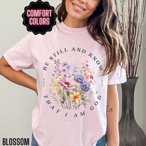 May include: A pink t-shirt with a floral design and the text "Be still and know that I am God" with the scripture reference "Psalm 46:10".