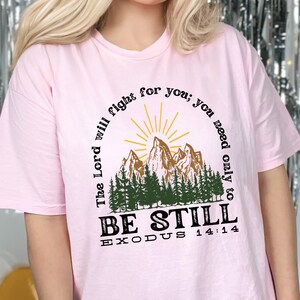May include: Pink t-shirt with a mountain scene and the text "The Lord will fight for you; you need only to BE STILL EXODUS 14:14"