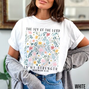 Op de afbeelding: Wit T-shirt met een bloemenpatroon en de tekst "The Joy of the Lord is My Strength, Nehemiah 8:10".