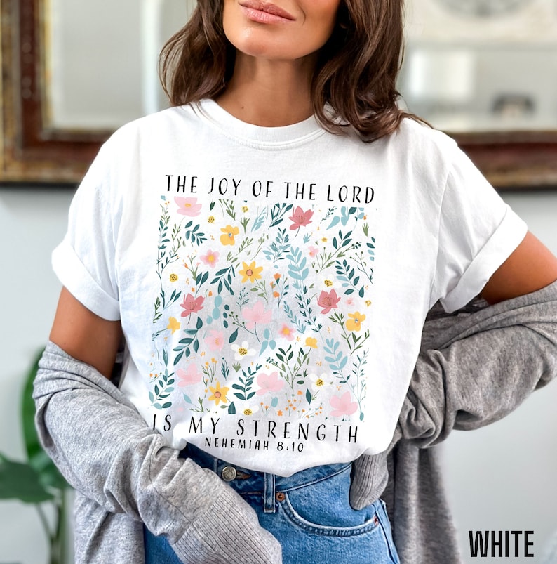 Op de afbeelding: Wit T-shirt met een bloemenpatroon en de tekst "The Joy of the Lord is My Strength, Nehemiah 8:10".