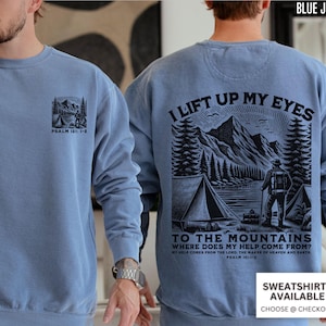 May include: A blue jean-colored sweatshirt with a mountain and tent graphic on the front and back. The front graphic includes the text "PSALM 121: 1-2". The back graphic features a mountain scene with the text "I LIFT UP MY EYES TO THE MOUNTAINS WHERE DOES MY HELP COME FROM?"