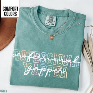May include: Light green t-shirt with the text "Professional Yapper" in rainbow colors. The shirt is made of a soft, comfortable material.