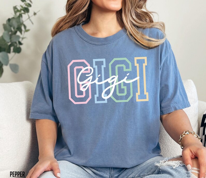 May include: A blue oversized t-shirt with the word "Gigi" in colorful block letters and a white cursive script.