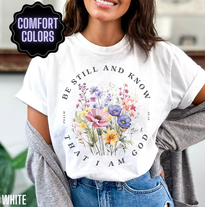 May include: White t-shirt with a floral design and the text "Be still and know that I am God" with the reference "Psalm 46:10".