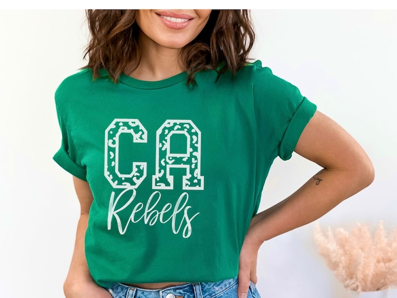 May include: A green t-shirt with the text "CA Rebels" in white. The letters "CA" are in a block letter style with a leopard print pattern. The word "Rebels" is in a cursive font.
