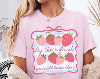 May include: Pink t-shirt with a graphic of strawberries and the text "By their fruit you will know them - Matthew 7:16"