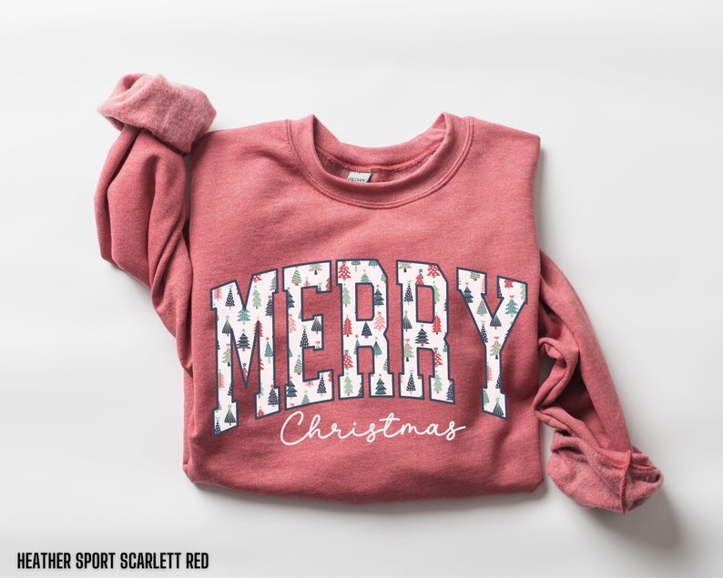 May include: A heather sport scarlett red sweatshirt with a white "Merry Christmas" graphic featuring a pattern of small Christmas trees.