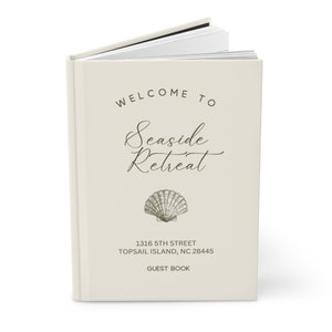 May include: A white guest book with the text "Welcome to Seaside Retreat" and a seashell illustration. The address "1316 5th Street, Topsail Island, NC 28445" and the words "Guest Book" are also printed on the cover.