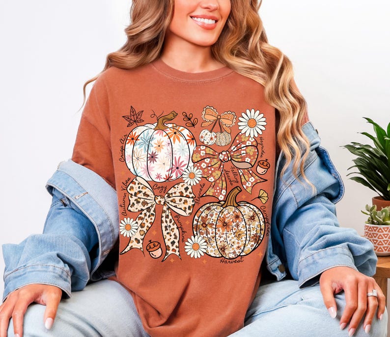 Puede incluir: Camiseta de color &oacute;xido con un gr&aacute;fico tem&aacute;tico de oto&ntilde;o. El dise&ntilde;o incluye calabazas, lazos y elementos florales. Tambi&eacute;n son visibles las palabras "Autumn Vibes", "Cozy" y "Harvest". La camiseta est&aacute; hecha de un material suave.