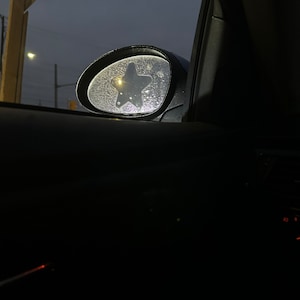 May include: A car's side view mirror with a star-shaped sticker on it. The mirror is covered in condensation droplets.