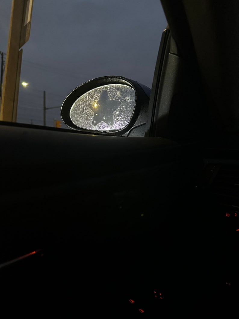 May include: A car's side view mirror with a star-shaped sticker on it. The mirror is covered in condensation droplets.