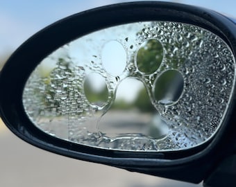 May include: A car's side mirror with a paw print sticker on it. The mirror is covered in condensation, creating a blurry effect.