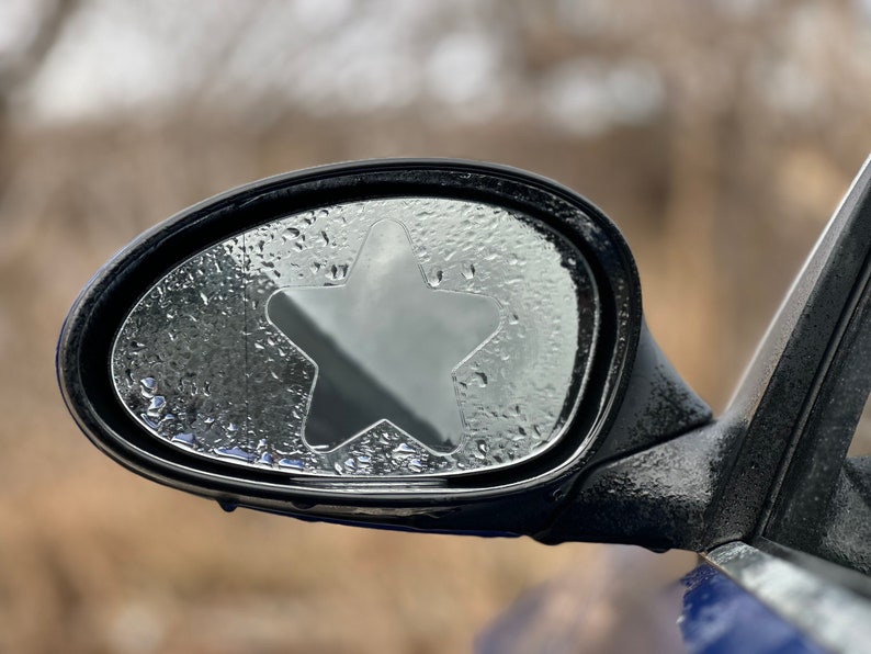 May include: A car side view mirror with a star-shaped rain guard. The mirror is covered in condensation droplets.