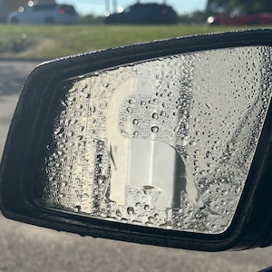 May include: A car's side view mirror with water droplets on the surface. The reflection in the mirror shows a blurry image of a car and a traffic light.