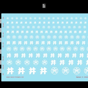 Op de afbeelding: Een lichtblauw vel met witte waterschuifstickers met rijen cirkelvormige bloemenemblemen en hekjesymbolen. Het vel bevat maataanduidingen van 2,5mm tot 8mm, met de tekst "Samurai - Ii - 2.5mm-8mm" en "angry-space-triangles.com" erop gedrukt.