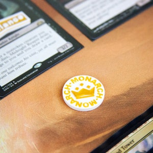 May include: A white round token with a yellow crown and the text "A-MONARCH" around the edge.